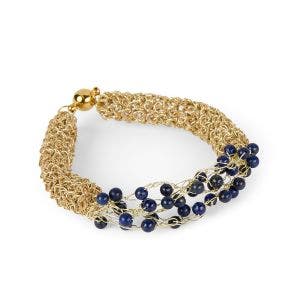 A gold bracelet made from gold wire with a edge covered in lapis lazuli stones.