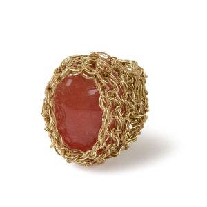 A side view of a crochet gold wire ring with a shiny orange agate stone in it's center.