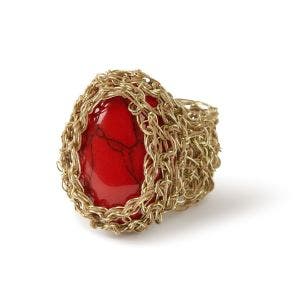 A side view of a oval red howlite set in gold wire.